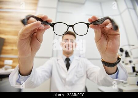 Déféruse POV prise de sourire optométriste mettant sur des lunettes sur un patient non reconnaissable pendant le test de vision dans la clinique moderne Banque D'Images