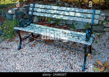 Banquette de jardin en métal peint noir avec les supports d'extrémité et des lattes de bois recouvertes de lichen debout sur le gravier, Cornwall, UK Banque D'Images