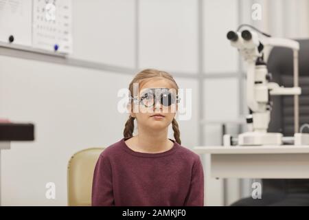 Portrait de la petite fille mignonne portant un cadre d'essai pendant le test de vision dans la clinique d'ophtalmologie pédiatrique, espace de copie Banque D'Images