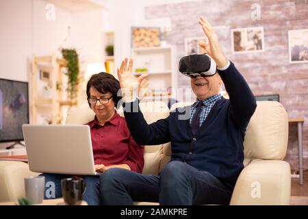 Personnes âgées à l'aide de l'homme retraite vieux casque de réalité virtuelle VR dans leur confortable appartement. Banque D'Images