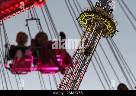 Passagers dans le carrousel à chaînes à la fête de la bière du soir, en arrière-plan la course Free Fall. [traduction automatique] Banque D'Images