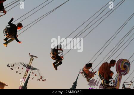 Passagers dans le carrousel à chaînes à la fête de la bière du soir, en arrière-plan, le tour Star Flyer. [traduction automatique] Banque D'Images