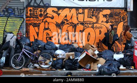 Les gens passent devant un tas de déchets sur un trottoir de New York avec des graffitis en arrière-plan et quelqu'un fouille dans les déchets, 12 janvier 2020. Banque D'Images