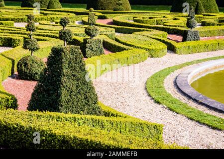 Un parterre dans un jardin à la française, avec des arbustes et des haies basses de buis taillés dans des formes géométriques, et un chemin de gravier blanc autour d'un bassin. Banque D'Images