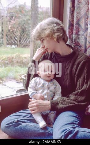 Jeune mère souffrant de dépression post-natale avec son bébé assis sur le plancher à côté des portes, à l'extérieur se sentir triste Banque D'Images