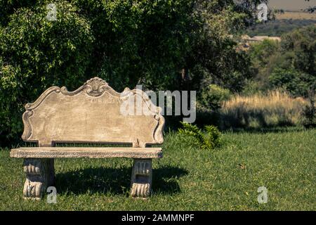 Photographie d'un banc de parc en béton sur la pelouse avec des arbres derrière. Banque D'Images