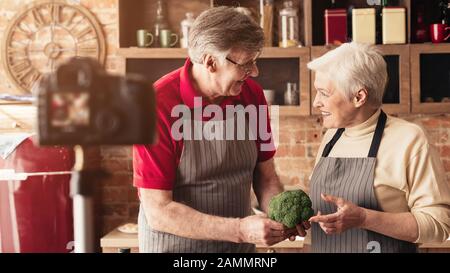 Des aînés souriants enregistrent la vidéo dans la cuisine, panorama Banque D'Images