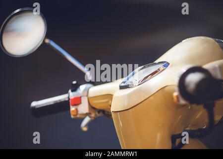 Le volant d'un cyclomoteur beige vintage avec tableau de bord et un rétroviseur rond est éclairé par une lumière vive. Banque D'Images