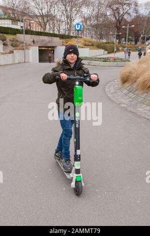 Garçon de dix ans qui monte un scooter électrique de location de chaux, Karlsplatz, Vienne, Autriche. Banque D'Images