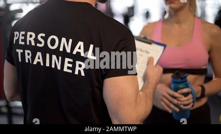 Entraîneur de forme physique expliquant le programme d'entraînement et le programme à la cliente féminine dans la salle de gym Banque D'Images