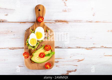 Toasts de pommes de terre douces avec avocat, œufs durs, tomates et graines de sésame sur carton en bois. Concept de repas sain. Cuisine propre, cuisine végétarienne, vue sur le dessus Banque D'Images