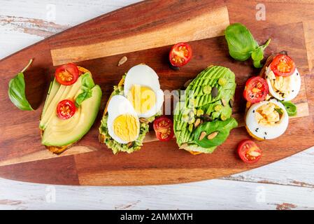 Toasts de pommes de terre douces avec avocat, œufs durs, tomates et graines de sésame sur carton en bois. Concept de repas sain. Cuisine propre, cuisine végétarienne, vue sur le dessus Banque D'Images