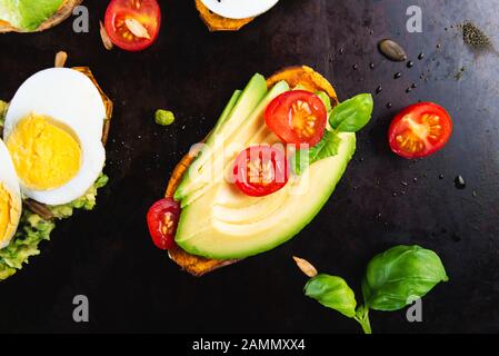 Toasts de patate douce avec avocat, œufs durs, tomates et graines de sésame sur fond sombre. Concept de repas sain. Cuisine propre, plats du Pescetarian, vue sur le dessus Banque D'Images