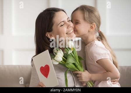 Petite fille embrassant la mère sur la joue, présentant des fleurs et des cadeaux Banque D'Images