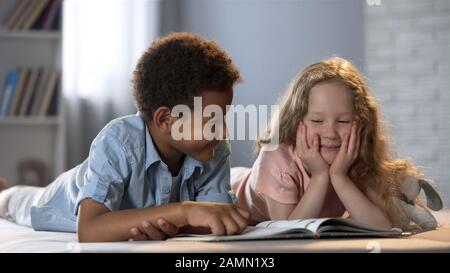 Petite fille et son ami afro-américain s'amuser tout en apprenant à lire le livre Banque D'Images