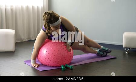 Une dame en surpoids qui essaie de faire des exercices sur le ballon de fitness, faisant des tentatives drôles Banque D'Images