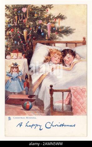 Carte postale originale de Noël traditionnelle mignonne d'enfants nichés dans le lit le matin de Noël avec des cadeaux et un arbre, huile originale, vers 1905, Angleterre, Royaume-Uni Banque D'Images