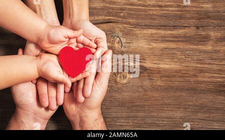 mains familiales tenant le cœur rouge sur fond de bois. Don, charité, concept de santé Banque D'Images