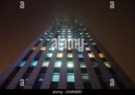 Un grand bâtiment avec la lumière dans les fenêtres se distingue dans le brouillard Banque D'Images