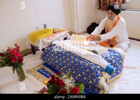 Un prêtre sikh assis lit à partir de la Sainte Écriture, le Gugru Granth Sahib. Dans un temple à Richmond Hill, Queens, New York. Banque D'Images