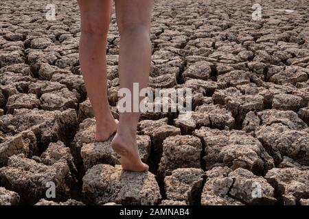 Les femmes marchant sur un sol fissuré et sec dans le paysage des zones arides, concept de crise de sécheresse Banque D'Images