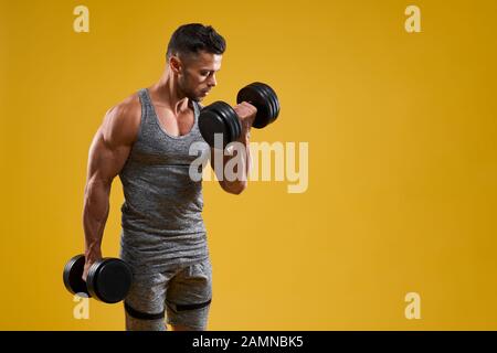 Vue latérale du beau bodybuilder athlétique poids lourds de levage. Strong guy brutale dans les vêtements de sport ce muscles. Isolé sur fond jaune studio avec copie espace. Concept de sport. Banque D'Images
