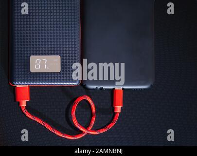 Chargement du smartphone avec la Power Bank noire via un câble USB sur fond noir. Vue de dessus. Banque D'Images