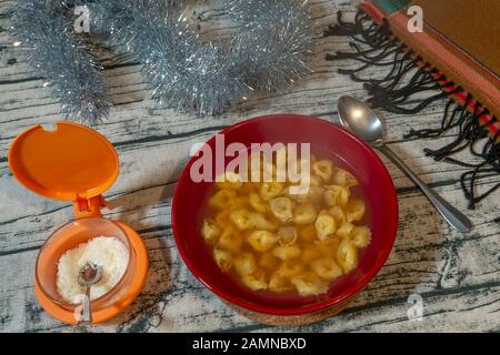 Bol rouge plein de délicieux tortellini dans le bouillon, plat typique de la cuisine italienne pour vous protéger du froid Banque D'Images