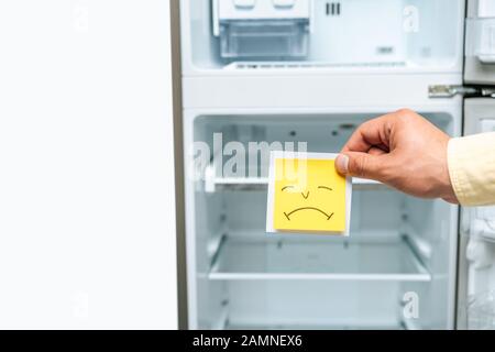 vue courte de l'homme tenant une sourit triste près de vide réfrigérateur ouvert isolé sur blanc Banque D'Images