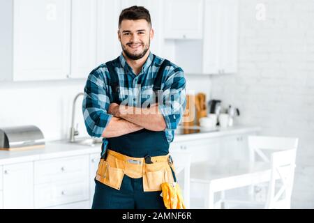 un homme heureux et barbu souriant tout en se tenant aux bras croisés Banque D'Images
