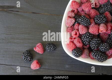 Fond de fruits frais et de baies. Mûres et framboises rouges. Mélangez les baies. Sur une plaque blanche sur un fond de table en bois noir. V Banque D'Images