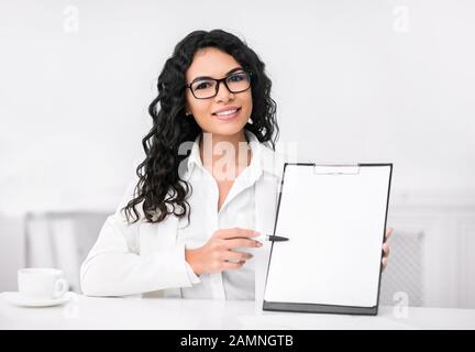 Smiling femme latine showing blank presse-papiers au bureau Banque D'Images