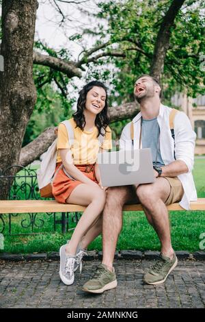 heureuse jeune femme assise sur un banc près de l'homme à l'aide d'un ordinateur portable Banque D'Images