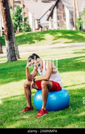 un sportif bouleversé assis sur un ballon de fitness bleu dans le parc Banque D'Images