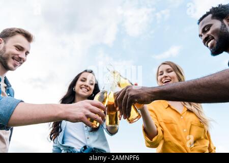 vue à bas angle des bonnes bouteilles de clinking multiculturelles pour hommes et femmes avec de la bière Banque D'Images