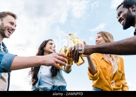 vue à bas angle des femmes et des hommes multiculturels gaies clinking bouteilles avec bière Banque D'Images