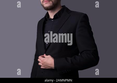 Un homme dans une veste noire, sur un fond gris foncé. Concept minimaliste. Espace libre vide. Portrait d'un jeune gars dans un costume d'affaires noir, tenant Banque D'Images