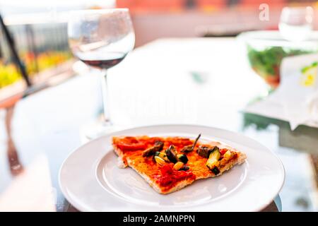 Une tranche de pizza sur la plaque blanche en Italie avec des légumes frais de sauce tomate et légumes hachés et un verre à vin rouge Banque D'Images