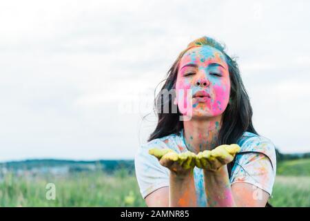 jeune femme séduisante avec des peintures holi colorées sur le visage regardant l'appareil photo et envoyer un baiser d'air Banque D'Images