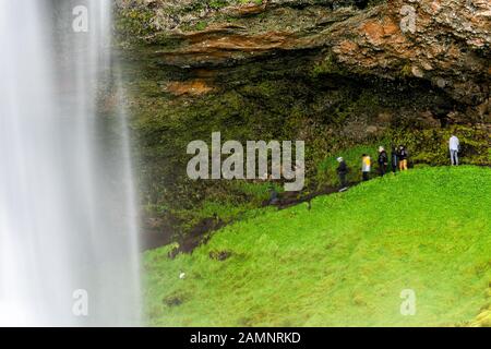 Gros plan de la cascade Seljalandsfoss longue exposition en Islande avec de l'eau blanche et des paysages d'été de mousse verte et des gens marchant sur la piste Banque D'Images