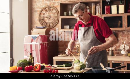 Grand-père soigneux préparant la salade dans la cuisine maison Banque D'Images