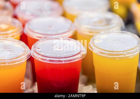 Gros plan de boisson au jus de jaune rouge cocktail tasses en plastique boissons et couverture dans le comptoir de magasin en été Banque D'Images