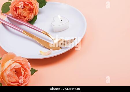 Plaque blanche avec la fourchette, couteau et fleurs rose sur fond pastel couleur pêche close-up. Banque D'Images