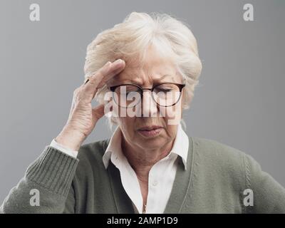 Vieille femme ayant un mal de tête, elle touche son front et se sent malade Banque D'Images
