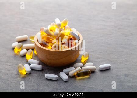 Assortiment dispersés médecine pharmaceutique comprimés, pilules, médicaments au bol en bois sur fond gris. Complément alimentaire aliments blancs écossés dur capsu Banque D'Images