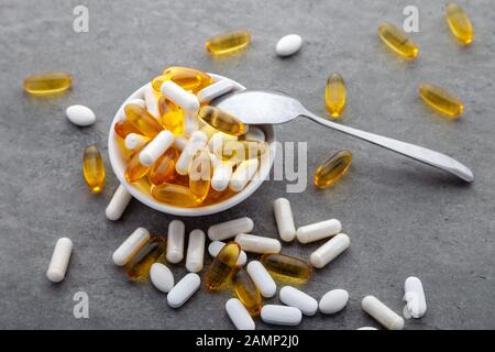 Médecine dispersés vitamines, pilules, médicaments au bol avec cuillère en métal sur fond gris. Complément alimentaire aliments blancs écossés dur rempli de capsules Banque D'Images