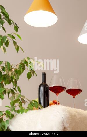 Bouteille sombre et deux verres de vin rouge sur la table de cuisine moderne, lampes sur table, feuilles vertes de l'arbre. La verticale. Copyspace. Place pour texte, lette Banque D'Images