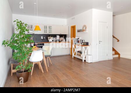 Intérieur moderne de cuisine confortable, salle à manger, mobilier blanc, mur, noir accessoires, matériaux naturels, des chaises en bois, vert fleur en pot. Concept Banque D'Images