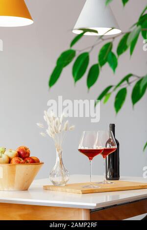 Bouteille sombre et deux verres de vin rouge, bol en bois avec des pommes, la décoration vase sur table dans une cuisine moderne, lampes sur table, feuilles vertes. La verticale. Cop Banque D'Images