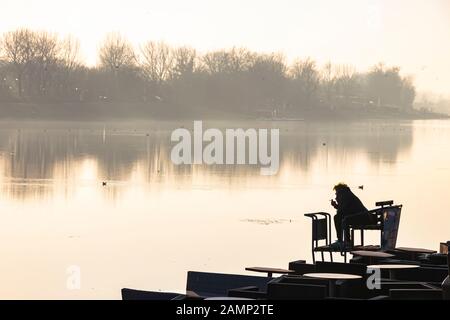 Silhouette d'une personne assise seule sur la rive de la rivière et fumer tout en regardant l'autre rive Banque D'Images